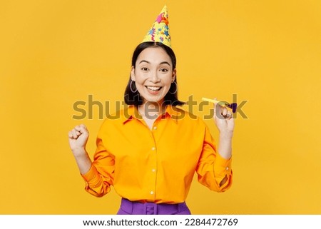 Happy fun excited overjoyed joyful young woman wear casual clothes celebrating holding in hand blowing pipe do winner gesture isolated on plain yellow background. Birthday 8 14 holiday party concept