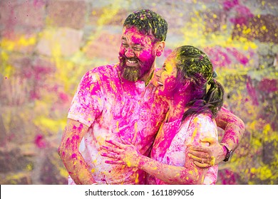 Happy fun loving asian indian couple painted in colors celebrating holi festival outdoor, love and relationship