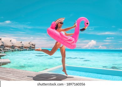 Happy Fun Luxury Hotel Vacation Woman Jumping Of Joy Taking Selfie With Pink Inflatable Swimming Pool Mattress At Overwater Bungalow Resort.