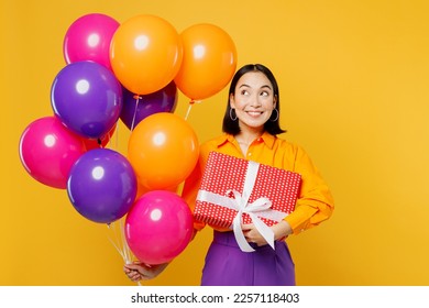 Happy fun smiling amazed young woman wear casual clothes celebrating look at balloons holding present box with gift ribbon bow isolated on plain yellow background. Birthday 8 14 holiday party concept - Shutterstock ID 2257118403