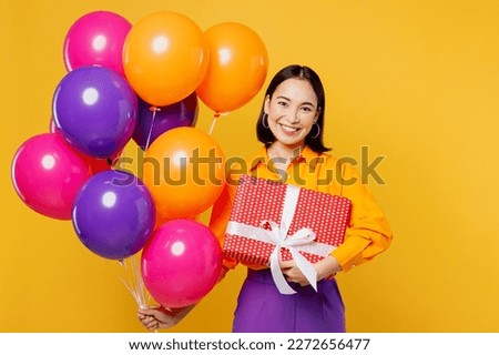 Happy fun smiling cheerful young woman wear casual clothes celebrating holding balloons present box with gift ribbon bow isolated on plain yellow wall background. Birthday 8 14 holiday party concept