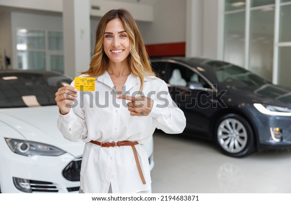 Happy fun woman customer buyer client in white\
shirt hold point on credit bank card choose auto want buy new\
automobile in car showroom vehicle salon dealership store motor\
show indoor Sales concept