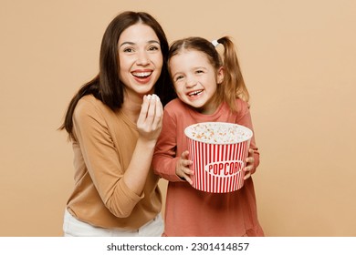 Happy fun women wear casual clothes with child kid girl 6-7 years old. Mother daughter watch movie film eat popcorn hold takeaway bucket isolated on plain beige background Family parent day concept - Powered by Shutterstock