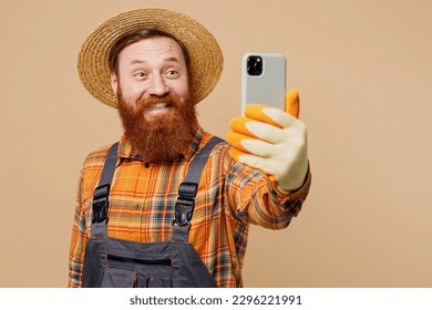 Happy fun young bearded man wear straw hat overalls work in garden doing selfie shot on mobile cell phone isolated on plain pastel light beige color background studio portrait. Plant caring concept - Powered by Shutterstock