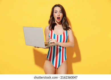 Happy Fun Young Sexy Woman Slim Body Wear Striped Red Blue One-piece Swimsuit Hold Laptop Pc Computer Isolated On Vivid Yellow Color Wall Background Studio. Summer Hotel Pool Sea Rest Sun Tan Concept