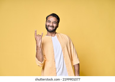 Happy funky cool indian man rocker punk hipster showing rock n roll heavy metal horns hand gesture screaming having fun advertising party festival isolated on yellow background. - Powered by Shutterstock