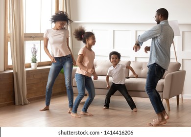 Happy Funny Active African American Family Of Four Parents And Cute Little Mixed Race Kids Dancing Laughing In Living Room, Black Mom Dad With Small Children Having Fun Together Enjoy Leisure At Home