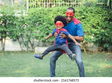 Happy funny African American father carrying little boy flying in superhero costume in garden at home. Happy loving Black African family playing together. Childhood and fun concept