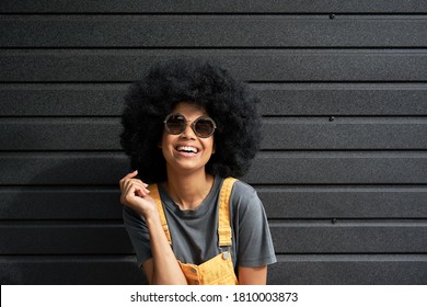 Happy funny African American young woman with afro hair wearing stylish sunglasses laughing standing against black wall background. Smiling fashion mixed race hipster in trendy eyewear portrait. - Powered by Shutterstock