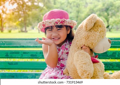 Happy And Funny Asia Little Girl 2- 3 Year Old Holding Teddy Bear  In Nature Park Outdoors. Looking At Camera.