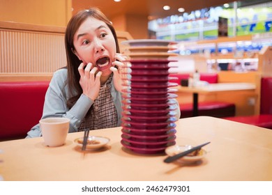 Happy funny Asian woman is counting a stacked Sushi plates on the dining table in Japanese conveyor belt Sushi bar and restaurant. - Powered by Shutterstock