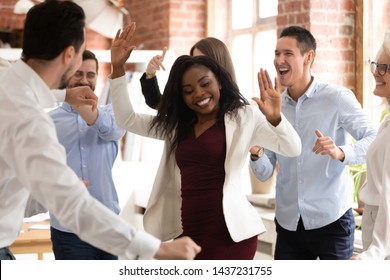 Happy funny black business woman with diverse team coworkers enjoy victory dance concept in office, multiracial friendly workers group dancing celebrate success having fun at corporate party together
