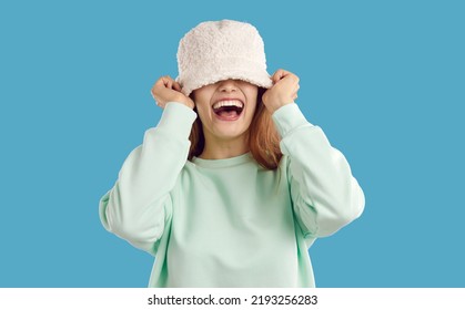 Happy funny carefree joyful young woman or teen girl with toothy smile puts on white cozy warm fluffy fuzzy artificial teddy lamb wool bucket hat that covers her eyes. Fashion concept Studio head - Shutterstock ID 2193256283