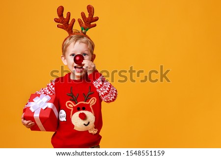 happy funny child boy in red Christmas reindeer costume with gift on yellow colored background
