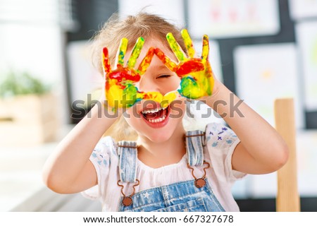 happy funny child girl draws laughing shows hands dirty with paint
