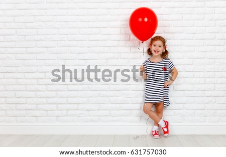 Happy funny child girl with a red ball near an empty white brick wall
