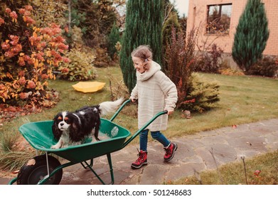 Happy Funny Child Girl Riding Her Dog In Wheelbarrow In Autumn Garden, Candid Outdoor Capture, Kids Playing With Pets