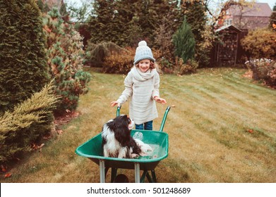 Happy Funny Child Girl Riding Her Dog In Wheelbarrow In Autumn Garden, Candid Outdoor Capture, Kids Playing With Pets