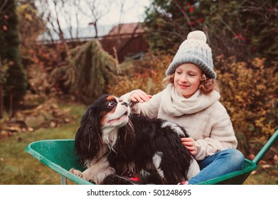 Happy Funny Child Girl Riding Her Dog In Wheelbarrow In Autumn Garden, Candid Outdoor Capture, Kids Playing With Pets