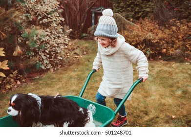 Happy Funny Child Girl Riding Her Dog In Wheelbarrow In Autumn Garden, Candid Outdoor Capture, Kids Playing With Pets