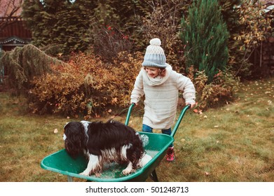 Happy Funny Child Girl Riding Her Dog In Wheelbarrow In Autumn Garden, Candid Outdoor Capture, Kids Playing With Pets