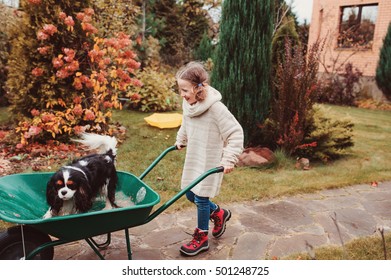 Happy Funny Child Girl Riding Her Dog In Wheelbarrow In Autumn Garden, Candid Outdoor Capture, Kids Playing With Pets