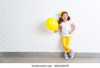 happy funny child girl with yellow air balloon near an empty brick wall