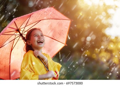 Happy funny child with red umbrella under the autumn shower. Girl is wearing yellow raincoat and enjoying rainfall. Kid playing on the nature outdoors. Family walk in the park. - Powered by Shutterstock