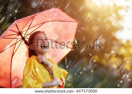 Happy funny child with red umbrella under the autumn shower. Girl is wearing yellow raincoat and enjoying rainfall. Kid playing on the nature outdoors. Family walk in the park.