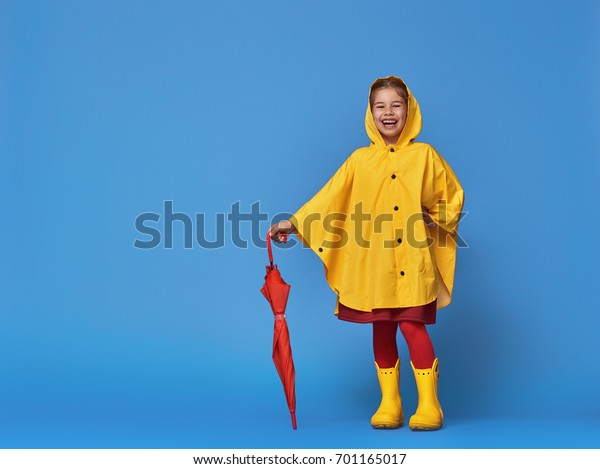 青の壁の背景にポーズを付けた赤い傘を持つ 幸せで面白い子ども 女の子は黄色のレインコートとゴムのブーツをはいている の写真素材 今すぐ編集