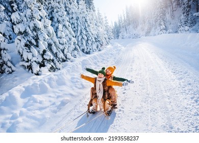 Niños felices y divertidos montan trineos retro de madera en un camino nevado en las montañas. Familia en la caminata invernal.
