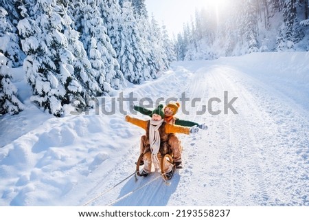 Happy funny children ride wooden retro sleds on snowy road in mountains. Family on winter walk.