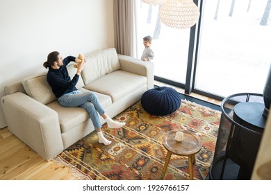 Happy Funny Father And Cute Little Child Son Laughing In Modern Living Room. Joyful Parent Dad Sitting At The Sofa And Holding Teddy Bear While Playing With Kid Boy Together. Fun And Home Concept