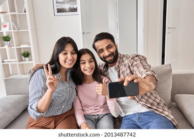 Happy Funny Indian Family With Teen Child Daughter Having Virtual Call Meeting On Modern Cellphone At Home. Smiling Dad Holding Cellphone Looking At Mobile Phone Taking Selfie, Recording Vlog With Kid