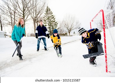 Happy Funny Kids Playing Hockey With Father And Mother On Street In The Winter Season