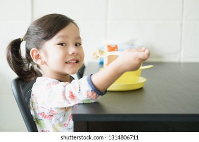 Happy Funny Little Asian Girl 2-3 Year Old Enjoy Eating Shrimp Wonton Soup With Yellow Container For Baby On Black Table And For Breakfast And Lunch