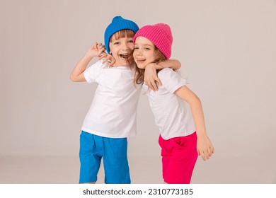 Happy, funny, little girl and boy, brother and sister in a blue and pink clothes on white background. Pink and blue knitted hats on the heads of children. Kids, children having fun on ski resort
