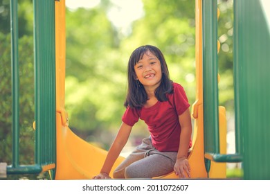 Happy Funny Little Girl Playing Merry Go Around At The Playground Outdoor In The Daytime Summer. Outdoor Activity. Playing Make Believe And Outside Education Concept.