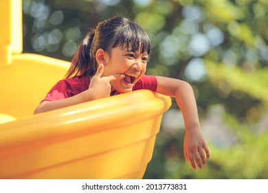 Happy Funny Little Girl Playing Merry Go Around At The Playground Outdoor In The Daytime Summer. Outdoor Activity. Playing Make Believe And Outside Education Concept.