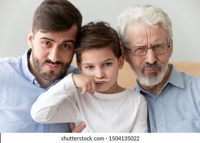 Happy funny multi 3 three generation men family close up portrait, cute child boy son grandson holding finger fake drawn moustache posing with young grown father and old grandfather look at camera