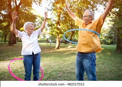 Happy And Funny Senior Couple Playing Hulahop In Park