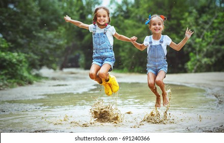 Happy funny sisters twins  child by girl jumping on puddles in rubber boots and laughing