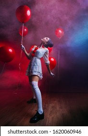 Happy funny Woman clown in old costume white knee high black retro boots, creative art bright makeup hairstyle two bun. Backdrop black gothic mystic room fog smoke, hold red balloon. 