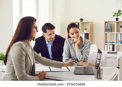 Happy future house buyers meeting real estate agent. Professional realtor talking to clients and offering flats options on computer. Smiling couple consulting bank worker or loan broker at her office