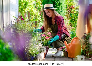 Happy Gärtnerin in Handschuhen und Schürze pflanzt Blumen auf dem Blumenbett im Garten. Gartenbau und Blumenzucht. Blumenpflege