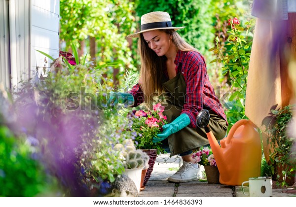 Happy gardener woman in gloves and apron plants\
flowers on the flower bed in home garden. Gardening and\
floriculture. Flower care