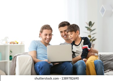 Happy Gay Couple And Adopted Child With Laptop At Home