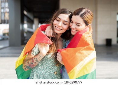 Happy gay couple cuddling with a rainbow flag around their shoulders and celebrating gay pride - Powered by Shutterstock