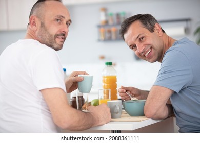 Happy Gay Couple Eating Breakfast In Kitchen