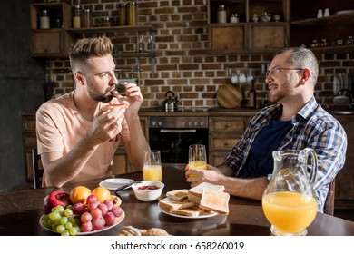 Happy Gay Couple Eating Breakfast And Looking At Each Other At Home